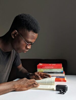 Young man studying intently with books in library setting.